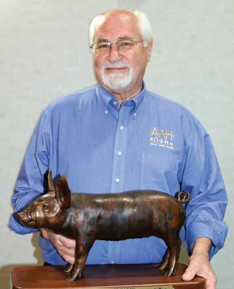 Dr. Henry standing behind dark copper-colored piglet statue