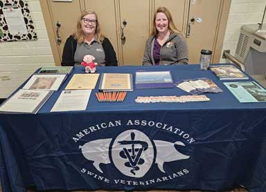 Two women seated behind a display table draped with the AASV banner