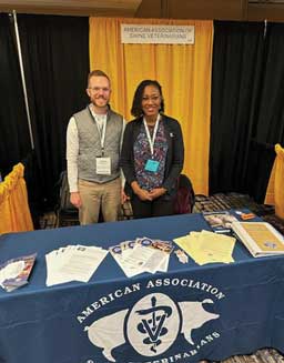 A man and a woman standing behind a display table draped with the AASV banner