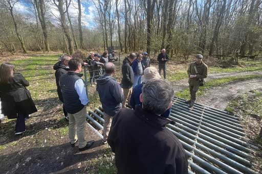 group of people observing a pipe grate inlaid in a dirt track in a lightly wooded area