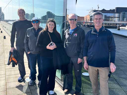 Five people standing outdoors on a city sidewalk in fron tof a structure with reflective glass walls