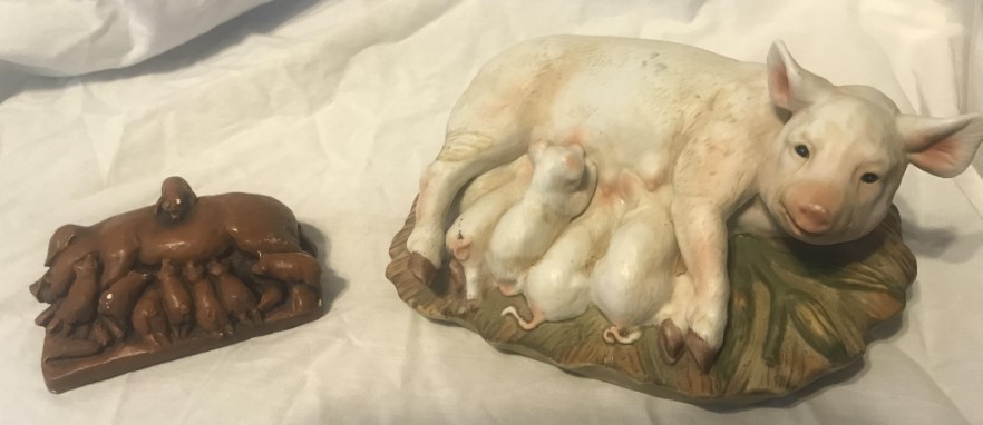 Two figurines of sows nursing piglets - one brown and a larger white one.